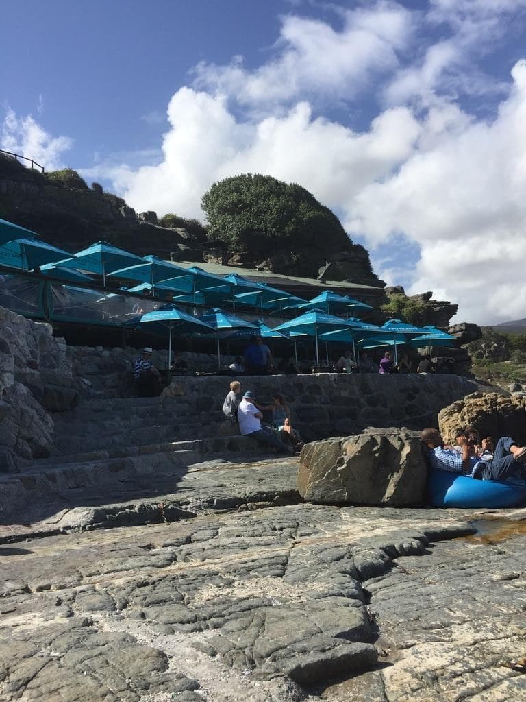 A coastal venue on the rocks, with rows of turquoise umbrellas above a stone terrace and the sea beyond