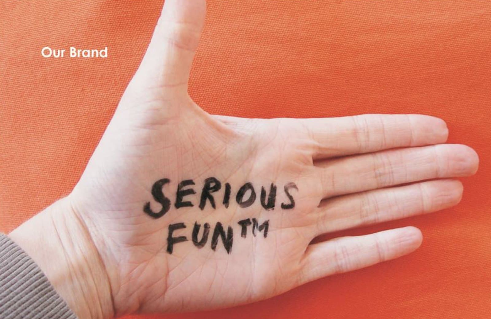 A hand with SERIOUS FUN written on the palm in marker, against an orange background